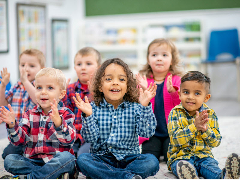 Happy kids sitting and clapping inside a school