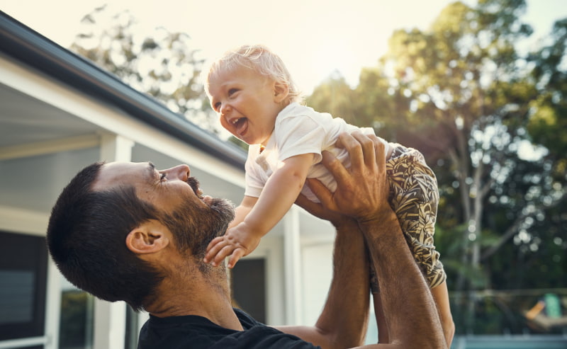 Father playing with his baby boy while standing outside his house